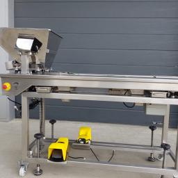 Inox Instal - Metalowa maszyna z podajnikiem i dwoma żółtymi pedałami nożnymi na tle szarej bramy garażowej.