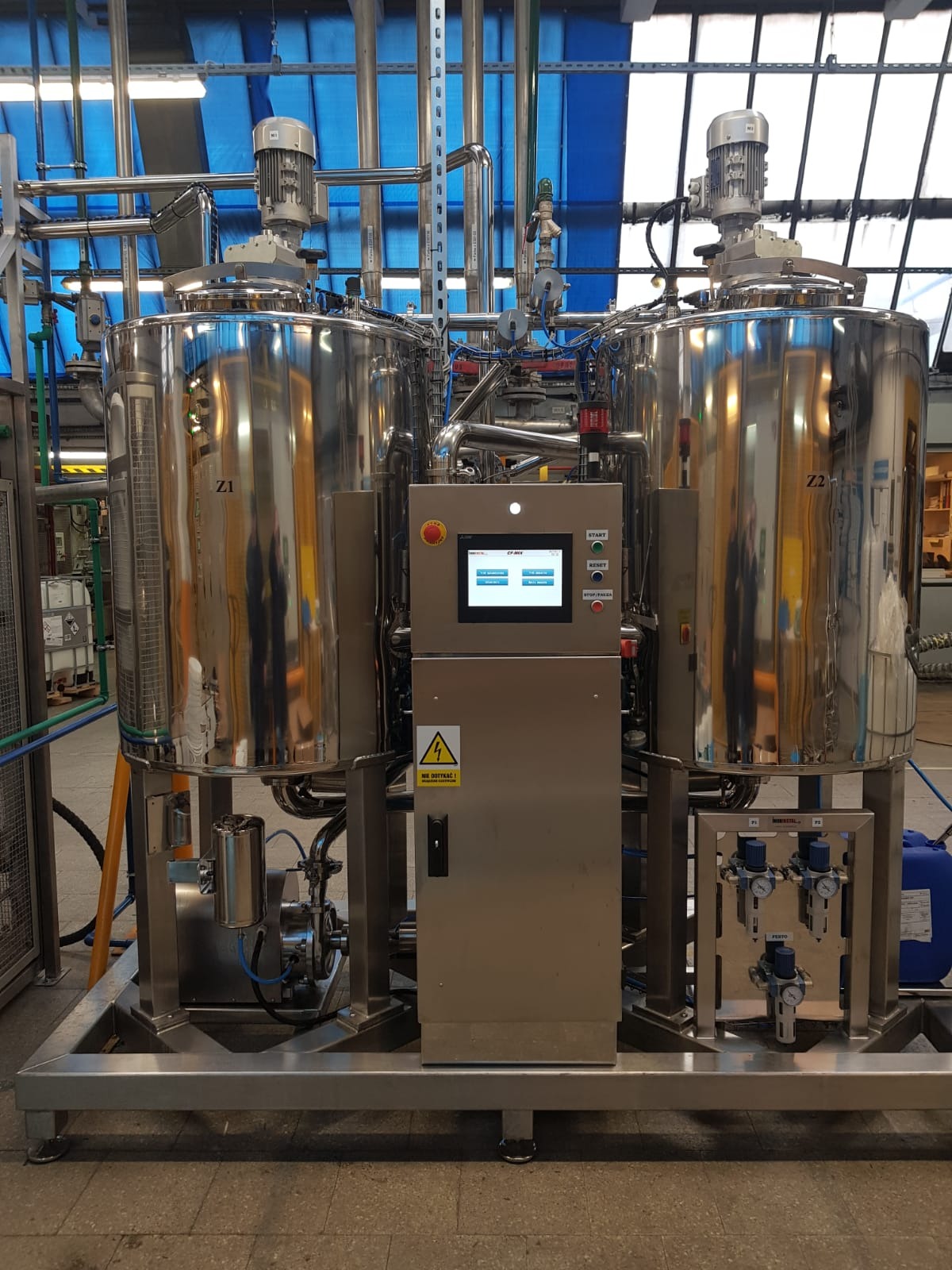 Dwa stalowe zbiorniki przemysłowe Z1 i Z2 z systemem rur i panelem sterowania, umieszczone na metalowej ramie w hali produkcyjnej.