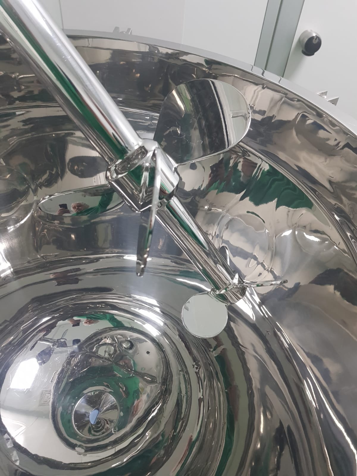 Wnętrze polerowanego zbiornika ze stali nierdzewnej z zamontowanym mieszadłem z trzema łopatkami, widoczne odbicia otoczenia.