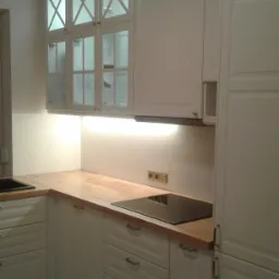 Nowoczesna kuchnia z białymi szafkami z przeszklonymi górnymi szafkami z motywem krzyża, drewnianym blatem i czarną płytą indukcyjną.