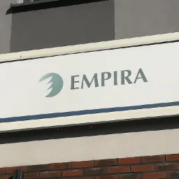 Szyld firmy Empira z zielonym logo na białym tle, umieszczony na elewacji budynku z ceglaną podstawą.