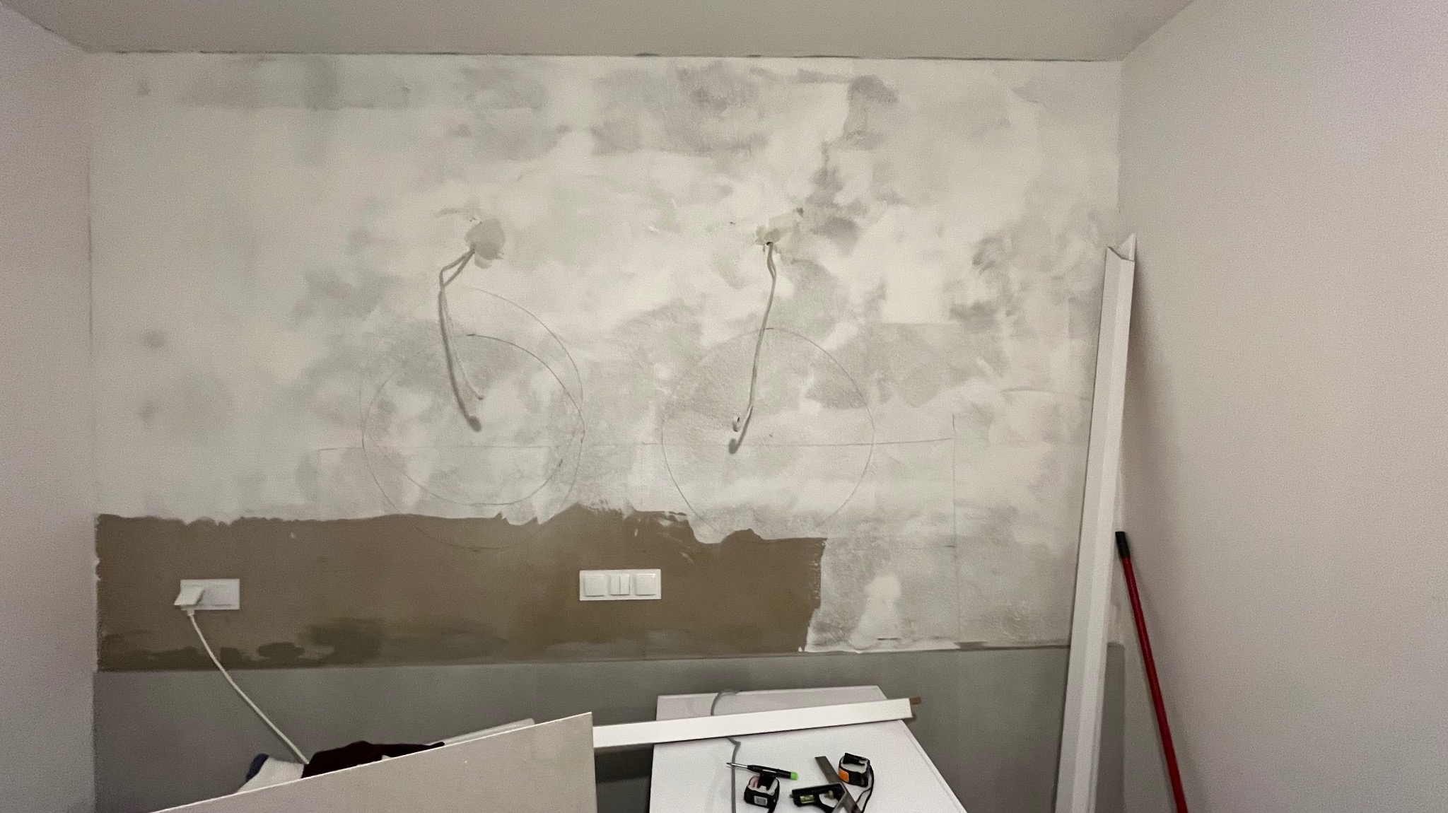 Łazienka w trakcie remontu: ściana z widocznymi przewodami, gniazdka i wyłączniki. Przygotowanie do montażu oświetlenia i wykończenia ściany. Widoczne narzędzia i materiały.