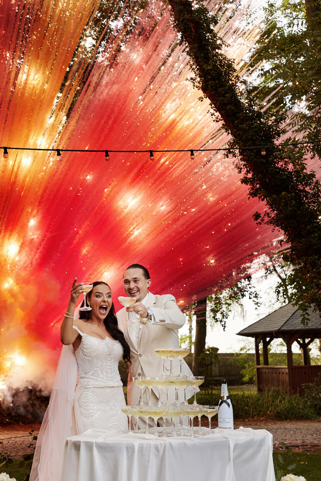 Para młoda w Świnoujściu wznosi toast szampanem na tle efektownych fajerwerków. Piramida z kieliszków, radosne emocje i dekoracje ślubne.