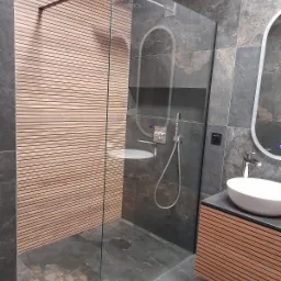 Nowoczesna łazienka z kabiną prysznicową typu walk-in, drewnianymi panelami na ścianie i szarą, kamienną okładziną, umywalką nablatową i podświetlanym lustrem.