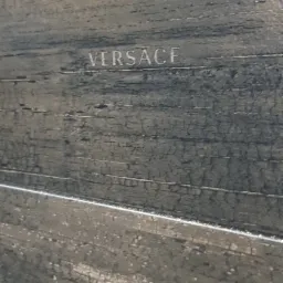 Płytka ceramiczna imitująca drewno z napisem VERSACE, widoczne delikatne spękania i struktura drewna.