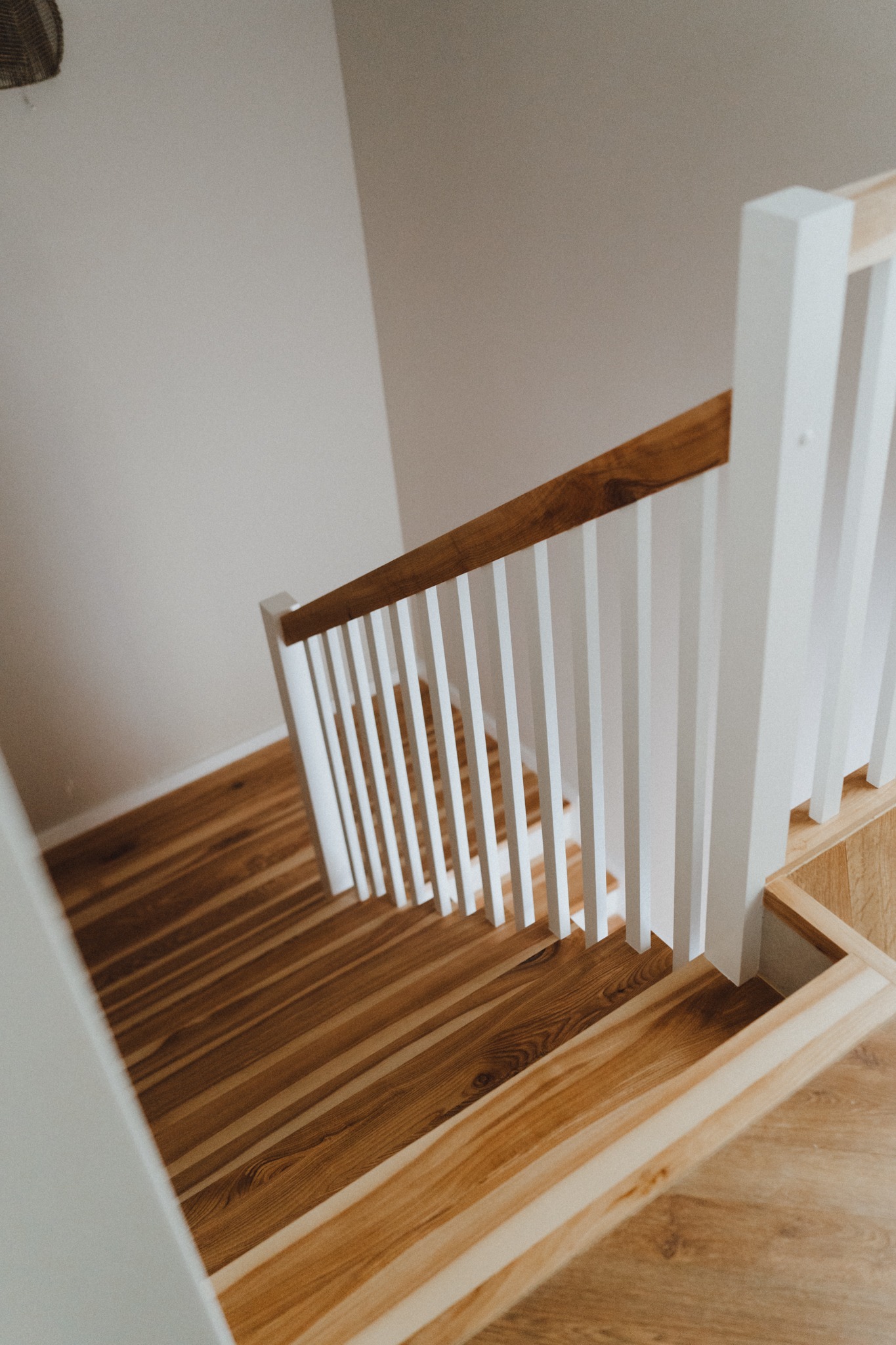 Widok z góry na drewniane schody z białymi balustradami, naturalne oświetlenie podkreśla usłojenie drewna.