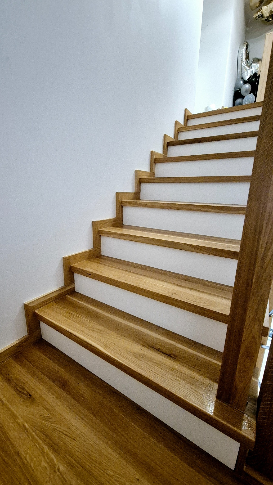 Jasne drewniane schody z białymi podstopnicami, widok z dołu, przy ścianie, z elementami dekoracyjnymi u góry