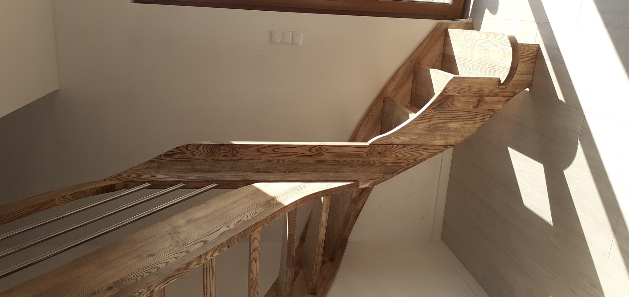 Jasne, drewniane schody z metalowymi poręczami, oświetlone promieniami słonecznymi, widok z góry.