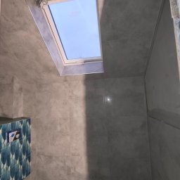 MK Remonty - Wykończenia - Szara łazienka w Limanowej z oknem dachowym i częściowo wykończoną ścianą z niebieskimi wzorzystymi płytkami, widoczne instalacje podtynkowe.