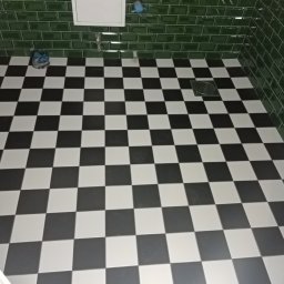MK Remonty - Wykończenia - Ukończona podłoga w łazience z czarno-białą szachownicą, zielone, błyszczące płytki na ścianach i odpływ liniowy w rogu.
