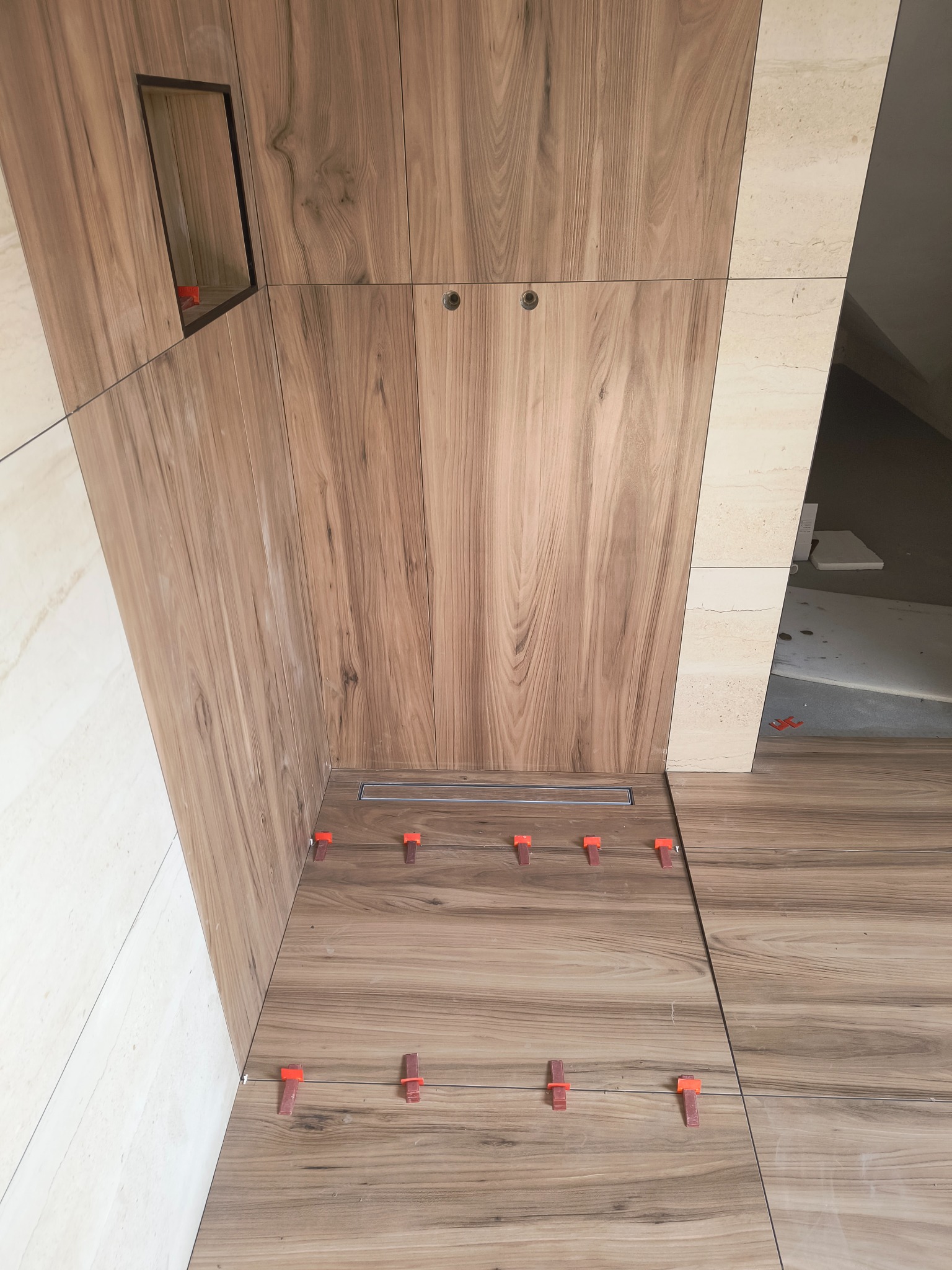 Wykończenie łazienki w Limanowej: Płytki imitujące drewno na ścianach i podłodze, z widocznym odpływem liniowym i elementami montażowymi.