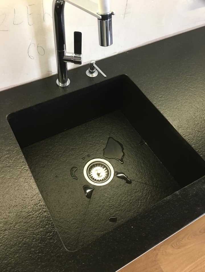Czarny, teksturowany blat kuchenny z wbudowanym zlewem i nowoczesną baterią z dozownikiem mydła; widoczne krople wody wokół odpływu.