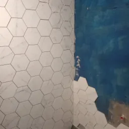 Układanie białych, marmurkowych płytek heksagonalnych na ścianie, z widocznymi krzyżykami dystansowymi, obok ściany pomalowanej na niebiesko, w trakcie prac wykończeniowych.