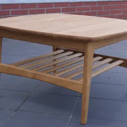 Stolik kawowy z jasnego drewna dębowego, z półką z listewek, na tle ściany z czerwonej cegły i szarej terakoty.