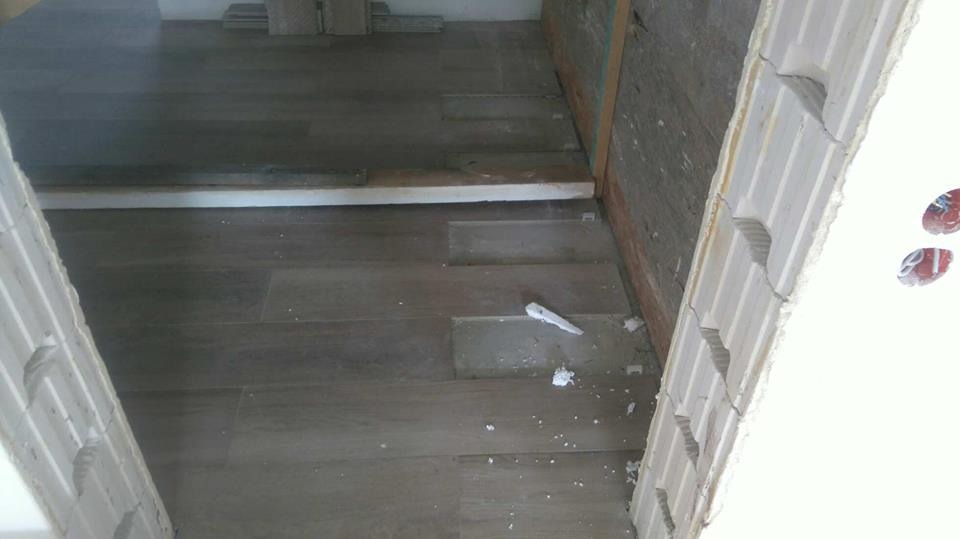 Układanie podłogi z płytek imitujących drewno w trakcie prac wykończeniowych, widoczne fragmenty ścian z białego gazobetonu i drewniane listwy przypodłogowe.