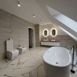 SOLIDNE WNĘTRZA - TOMASZ KIJOWSKI - Przestronna, jasna łazienka na poddaszu z wolnostojącą wanną, umywalkami z podświetlanymi lustrami owalnymi, białą ceramiką i płytkami imitującymi marmur.
