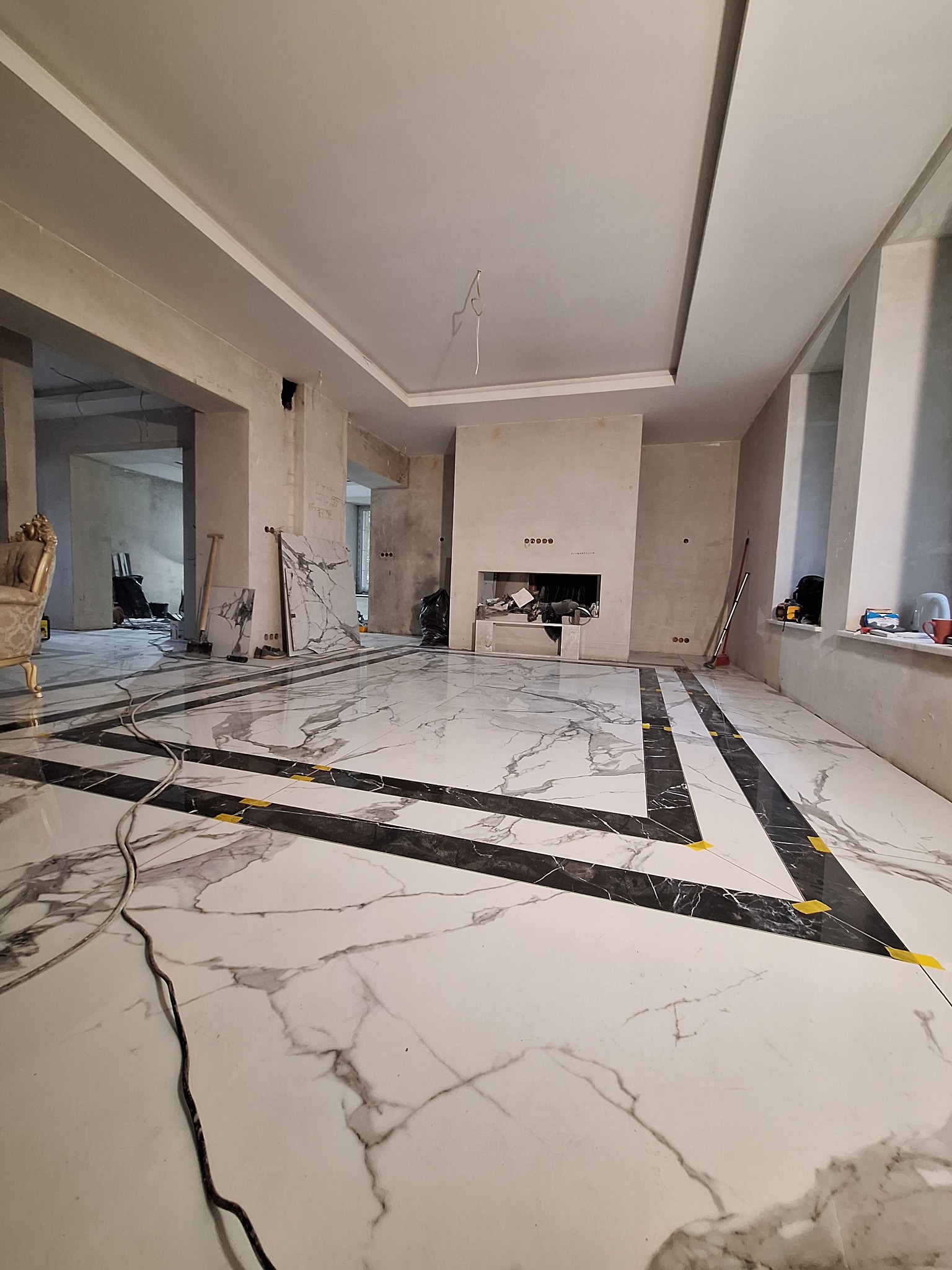Wnętrze w trakcie prac wykończeniowych: marmurowa podłoga z czarnymi intarsjami, surowe ściany i przygotowane miejsce na kominek.