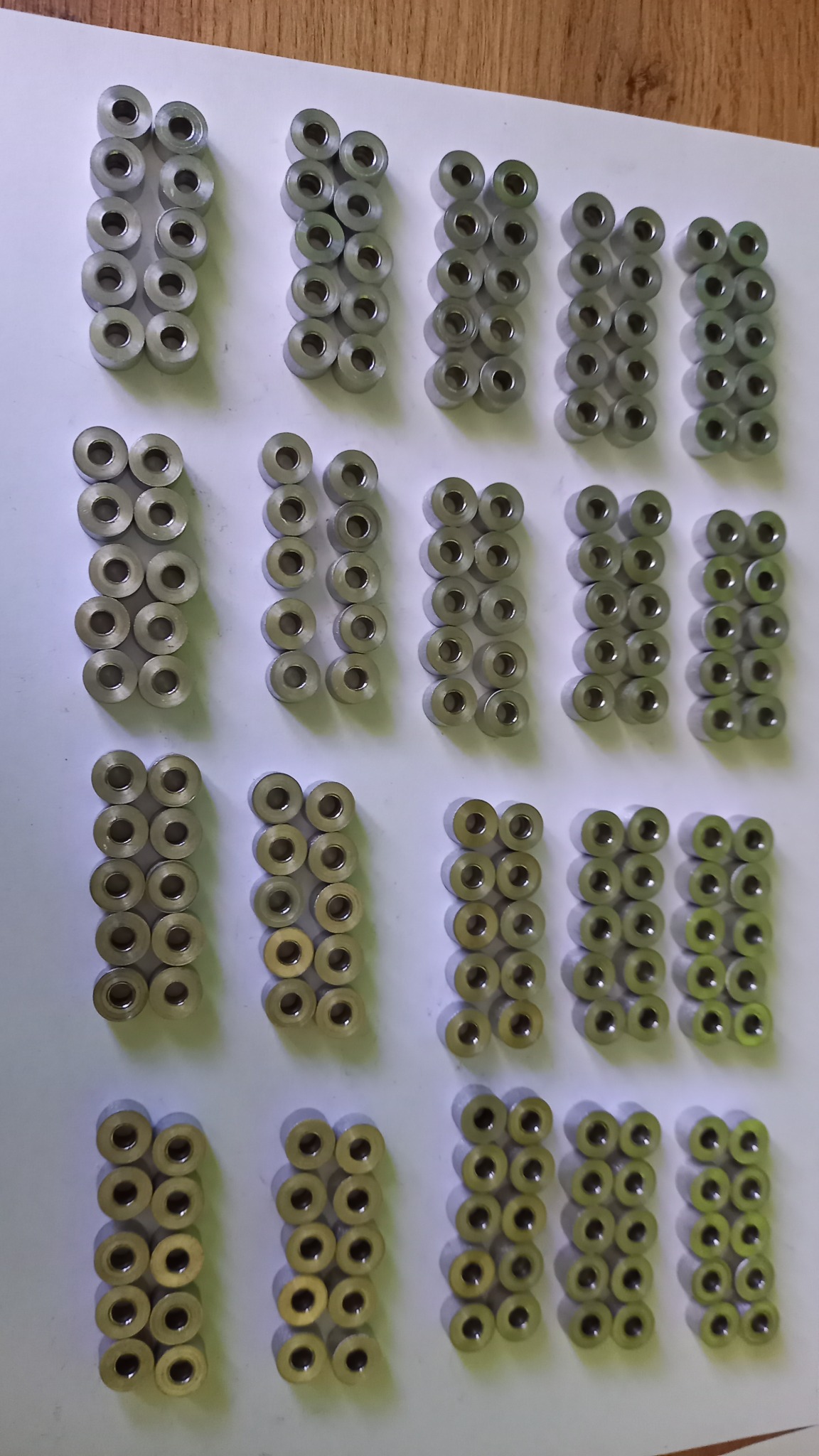 Partie identycznych, metalowych tulejek ułożonych w regularnych rzędach na białym tle, z widocznymi śladami obróbki.