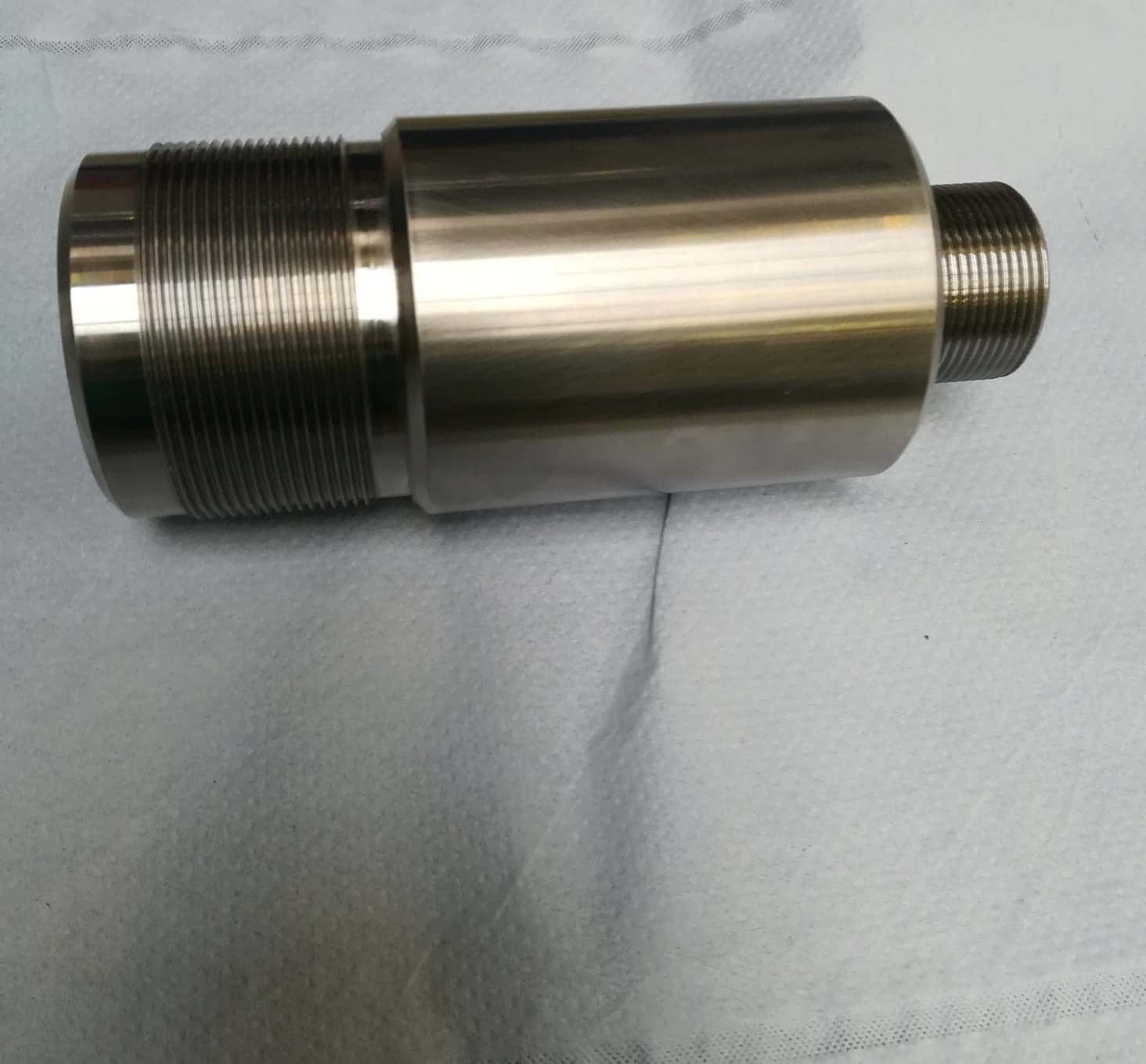 Cylindryczny, metalowy element z gwintem, leżący na szarym tle. Widoczne precyzyjne nacięcia gwintu i gładka powierzchnia.