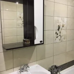 Wykończona łazienka w Siedlcach z beżowymi płytkami z motywem kwiatowym, umywalką, lustrzaną szafką z półką i widoczną wanną.