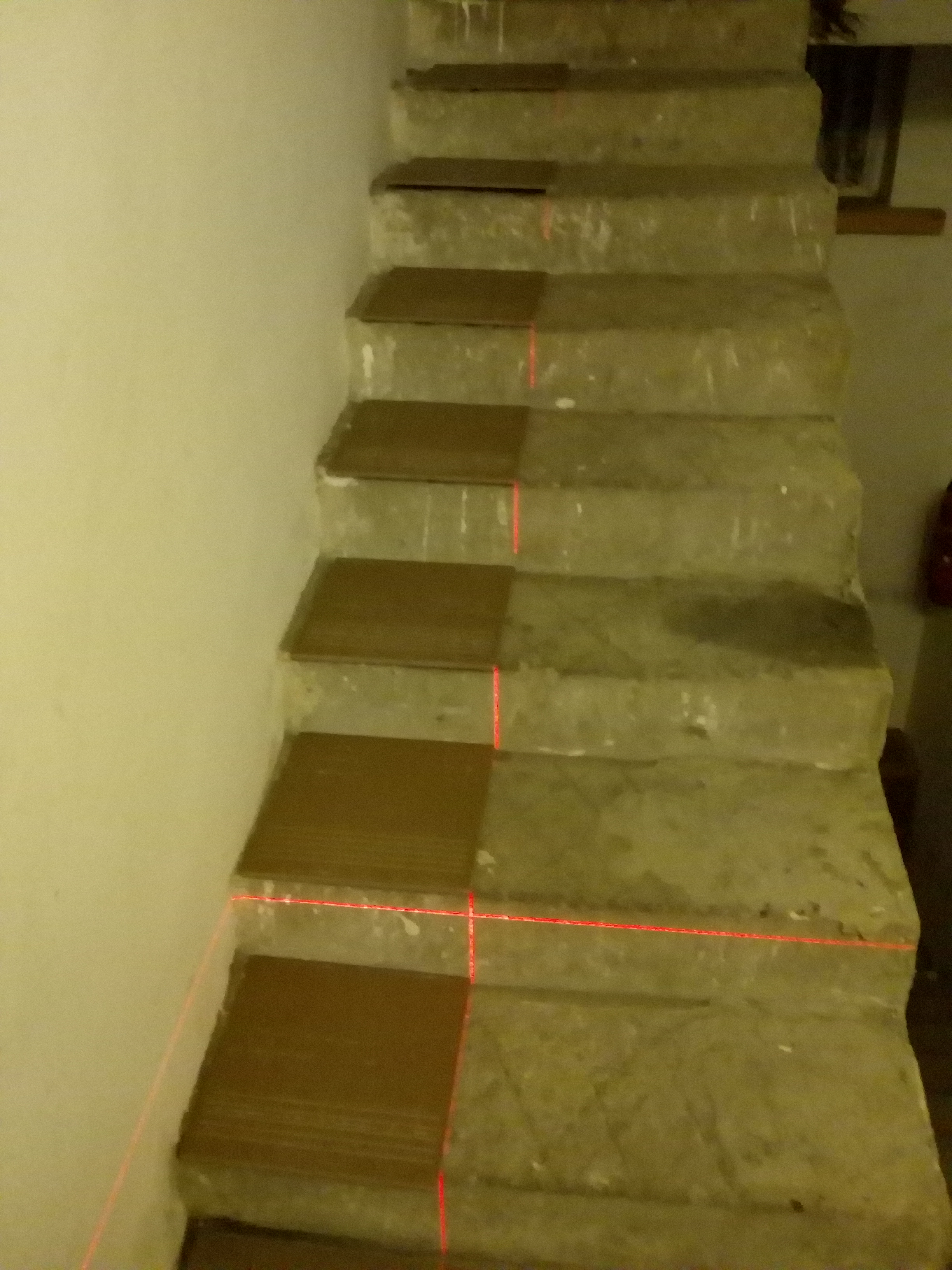 Renowacja schodów betonowych z częściowo położonymi brązowymi płytkami, wyznaczona laserem linia pozioma i pionowa, widok z góry w trakcie remontu.