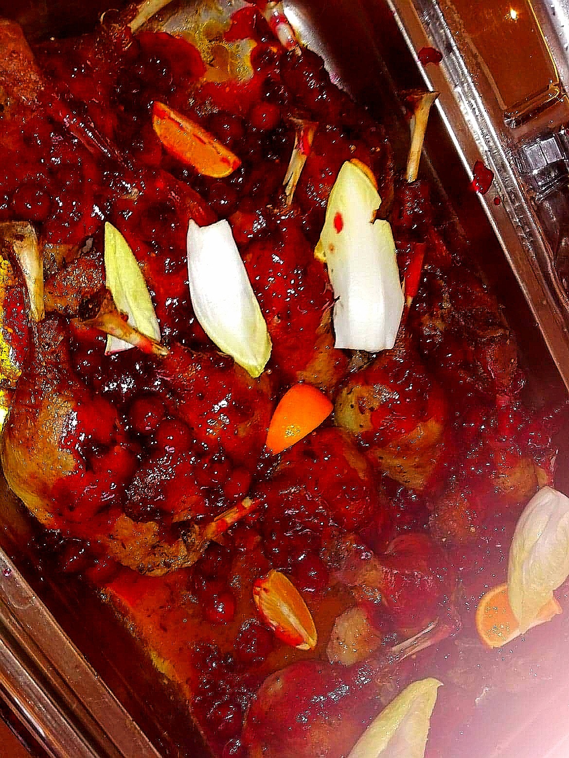 Pieczone udka kacze w gęstym czerwonym sosie żurawinowym, udekorowane plastrami pomarańczy i listkami endywii, serwowane w metalowej brytfannie.