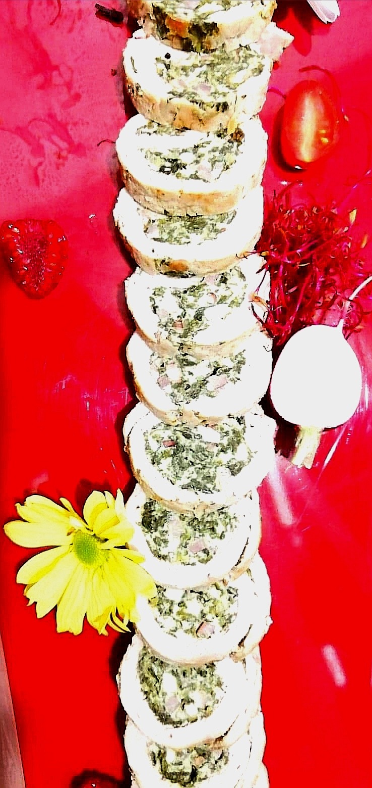 Ułożone w pionie roladki z nadzieniem szpinakowym, udekorowane kwiatem, połówką pomidora, rzodkiewką i kiełkami na czerwonym tle.