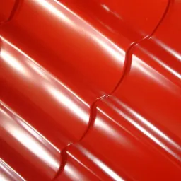 Czerwona blachodachówka modułowa z widocznymi przetłoczeniami i połyskiem, ułożona pod kątem, oświetlona z góry.
