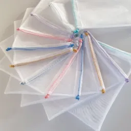 Stos białych, siateczkowych woreczków ze sznurkami w pastelowych kolorach, ułożonych wachlarzowo na jasnym tle.