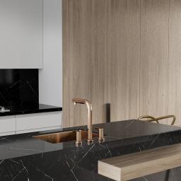 KGM Design Group - Nowoczesna kuchnia z czarnym marmurowym blatem, miedzianą armaturą i drewnianymi elementami, oświetlona wiszącymi lampami z miedzianymi akcentami. Na blacie leżą dekoracyjne kulki.
