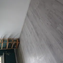 Świeżo pomalowane wnętrze z szarą podłogą imitującą drewno, białą górną częścią ściany i turkusową dolną częścią, widoczny metalowy grzejnik i drewniany regał.