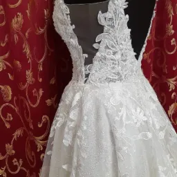 Detal koronkowego wykończenia sukni ślubnej na manekinie, z czerwonym, wzorzystym tłem.