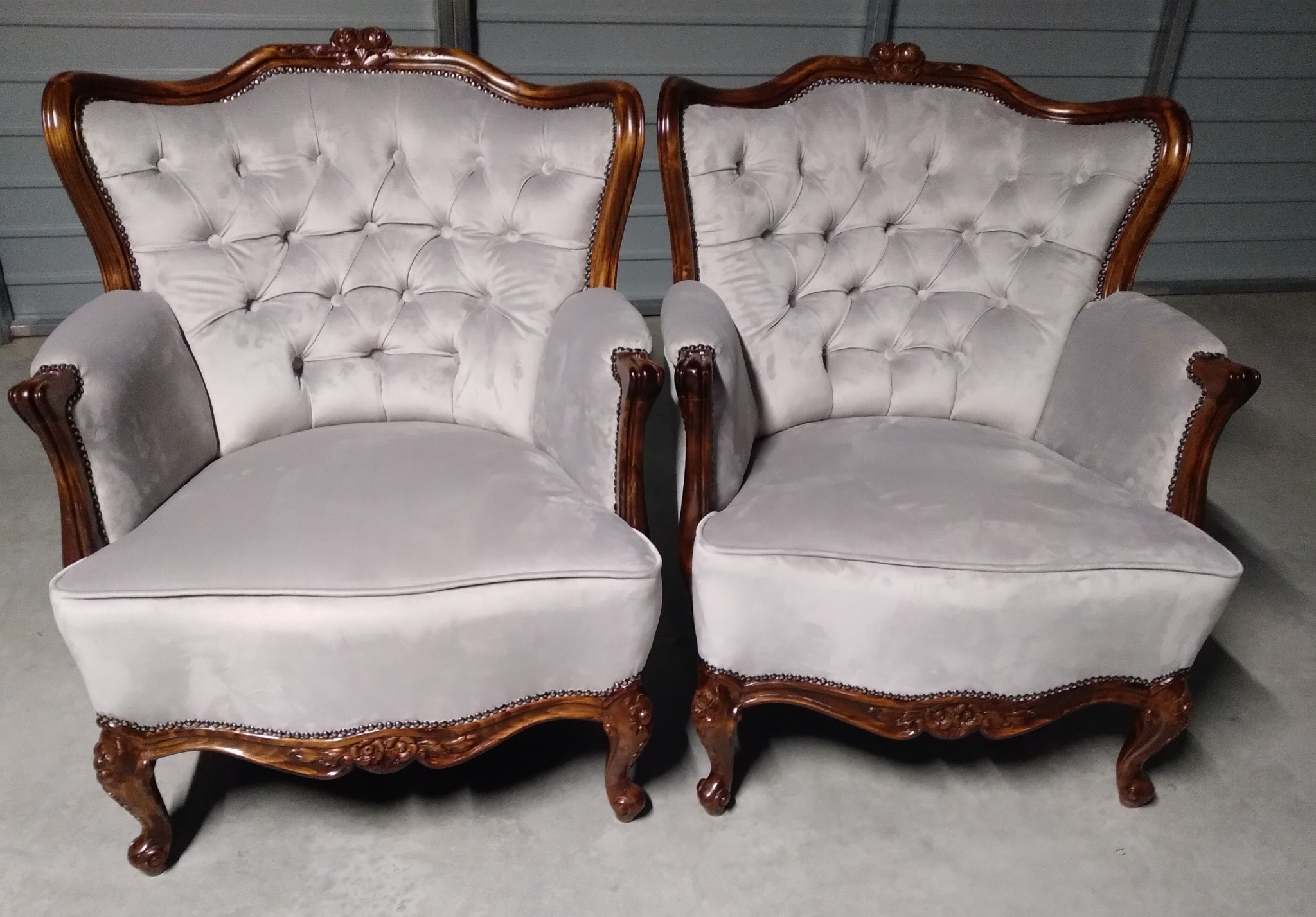 Dwa identyczne, odnowione fotele w stylu Ludwika XVI, obite szarym welurem z pikowaniem, z ciemnobrązowymi, rzeźbionymi nogami i ramami, ustawione obok siebie na szarym tle.