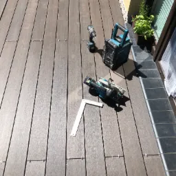 Montaż brązowego podestu z desek kompozytowych: wkrętarka, piła, radio budowlane i kątownik leżą na częściowo ułożonej powierzchni.