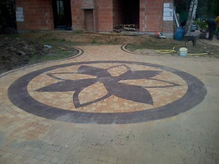 Ułożona kostka brukowa tworząca okrągły wzór kwiatowy na podjeździe przed budynkiem w trakcie budowy.