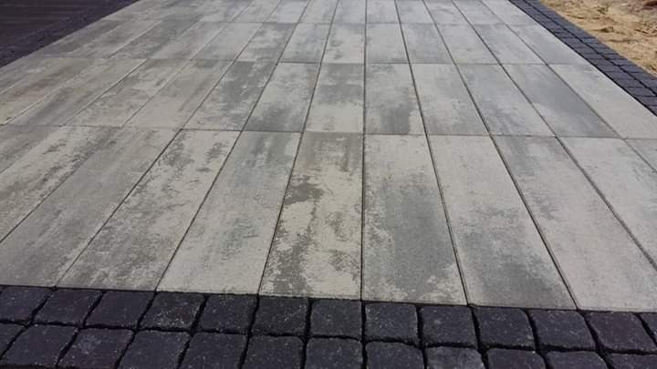 Ułożona nawierzchnia z prostokątnej kostki brukowej w odcieniach szarości, obramowana ciemną kostką na krawędziach. Widoczna faktura i wzór na powierzchni kostki.