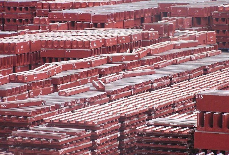 Stos czerwonych, betonowych korytek kablowych z oznaczeniami, ułożonych warstwami na placu składowym.