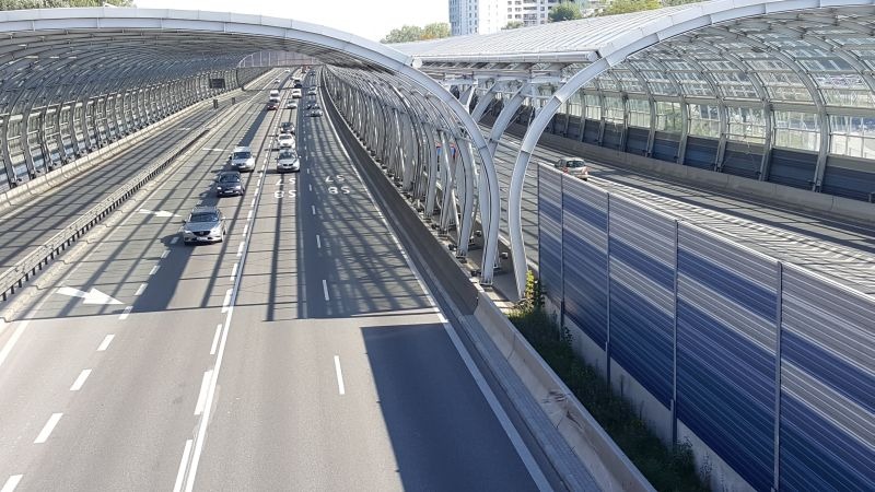 Autostrada z ekranami akustycznymi i zadaszeniem w formie łukowych konstrukcji stalowych, widok z góry na ruch samochodowy.