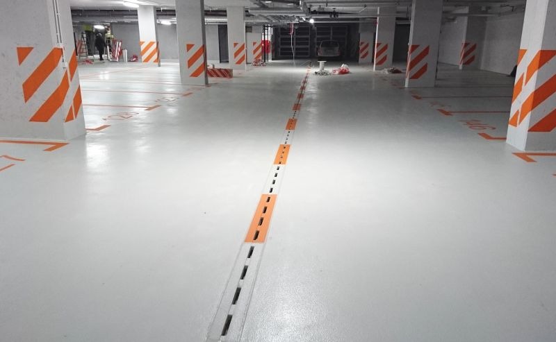 Oznakowane, białe podziemne miejsce parkingowe z pomarańczowymi pasami na filarach i numerami miejsc