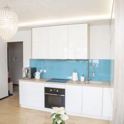 Meble Muzyka - Nowoczesna, jasna kuchnia z białymi szafkami, turkusowym panelem szklanym, drewnianym blatem i ozdobnym żyrandolem w kształcie kuli.