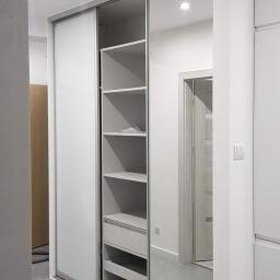 Meble Muzyka - Wnętrze z zabudowaną szafą przesuwną z lustrzanymi drzwiami i otwartą częścią z półkami i szufladami w szaro-białej kolorystyce.