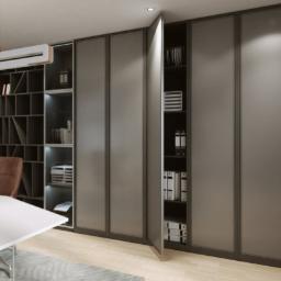 Meble Muzyka - Szafa przesuwna z szarymi, matowymi frontami, częściowo otwarta, z widoczną zawartością półek: segregatory i książki, w tle biurko i regał z książkami, oświetlenie LED wewnątrz szafy, logo firmy...