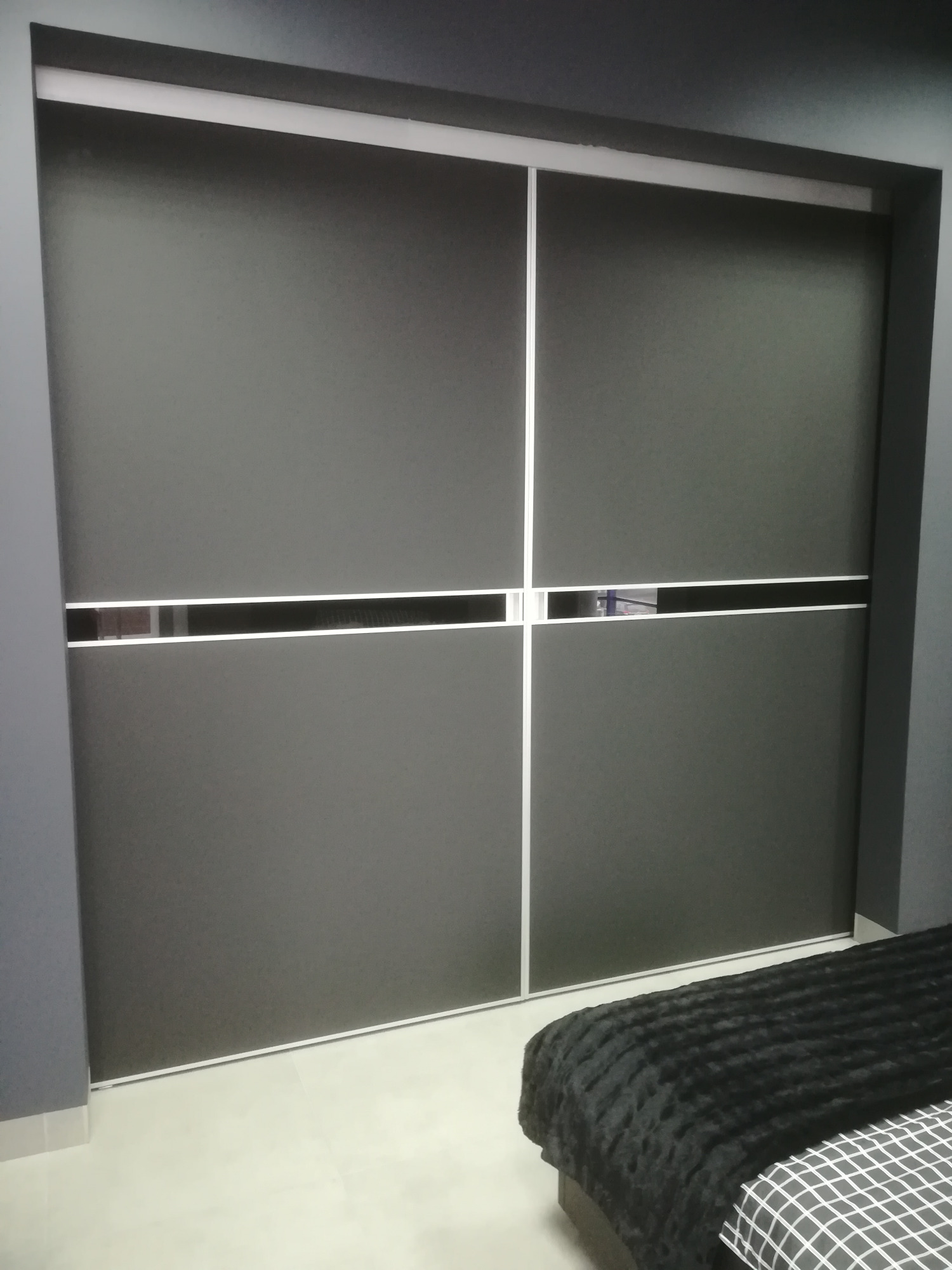 Nowoczesna szafa przesuwna w kolorze grafitowym z białymi akcentami, widoczna częściowo z boku łóżka z czarno-białą pościelą.