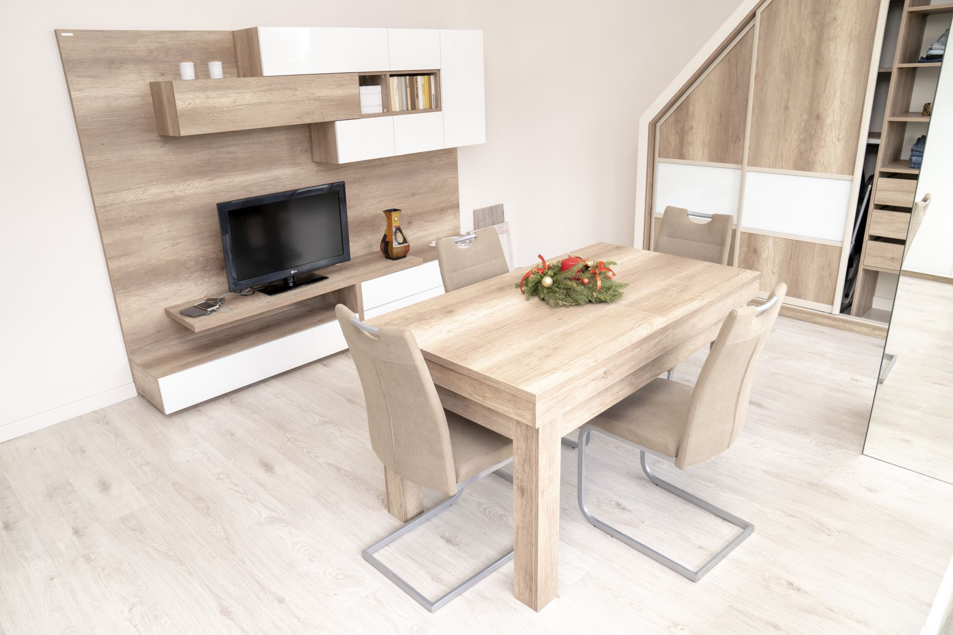 Jasne wnętrze jadalni z drewnianym stołem i krzesłami, na stole stroik świąteczny, w tle meble RTV z telewizorem oraz szafa przesuwna na poddaszu.
