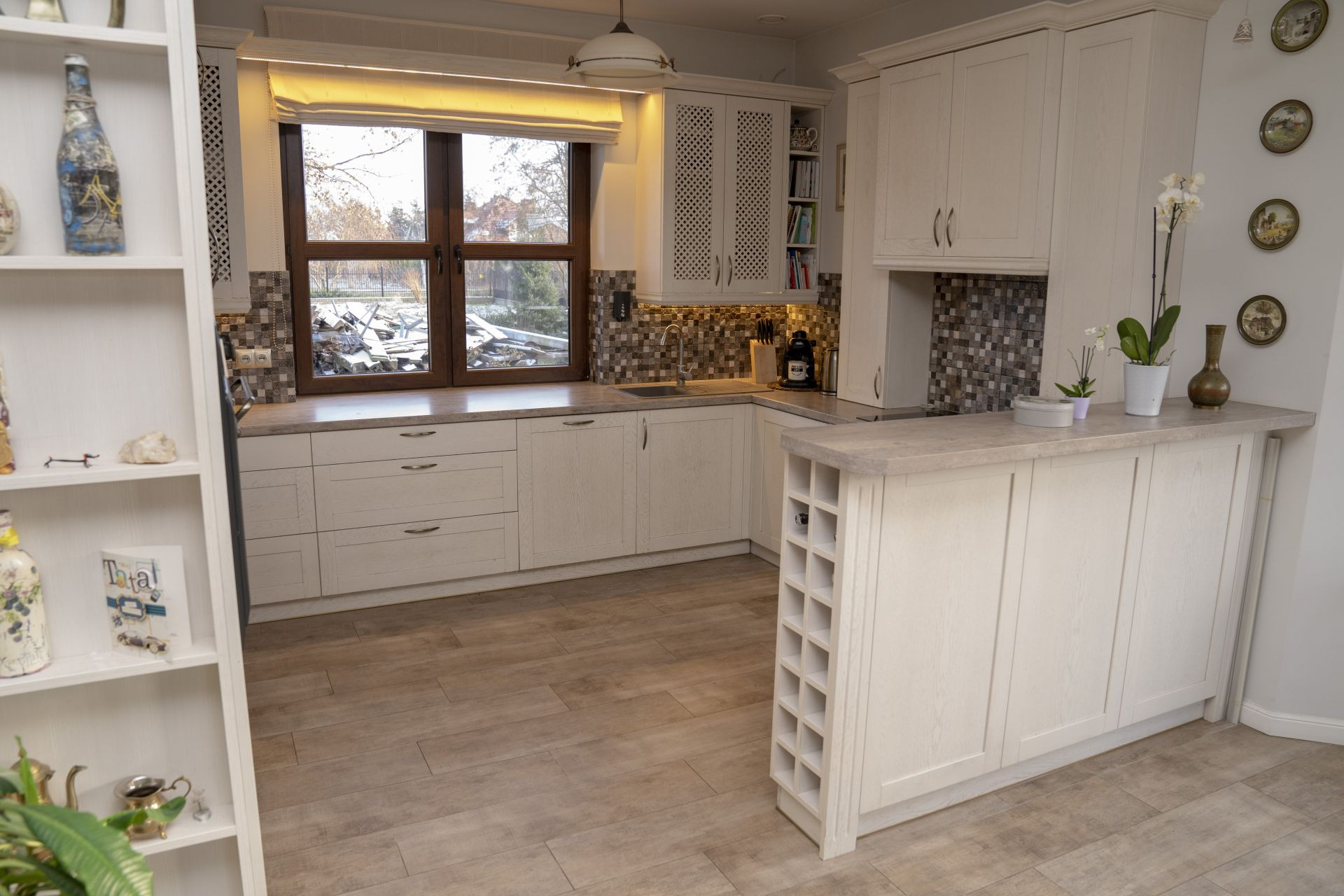 Jasna kuchnia z drewnianymi frontami, mozaiką nad blatem i oknem z widokiem na ogród, z półwyspem z wbudowanym regałem na wino.