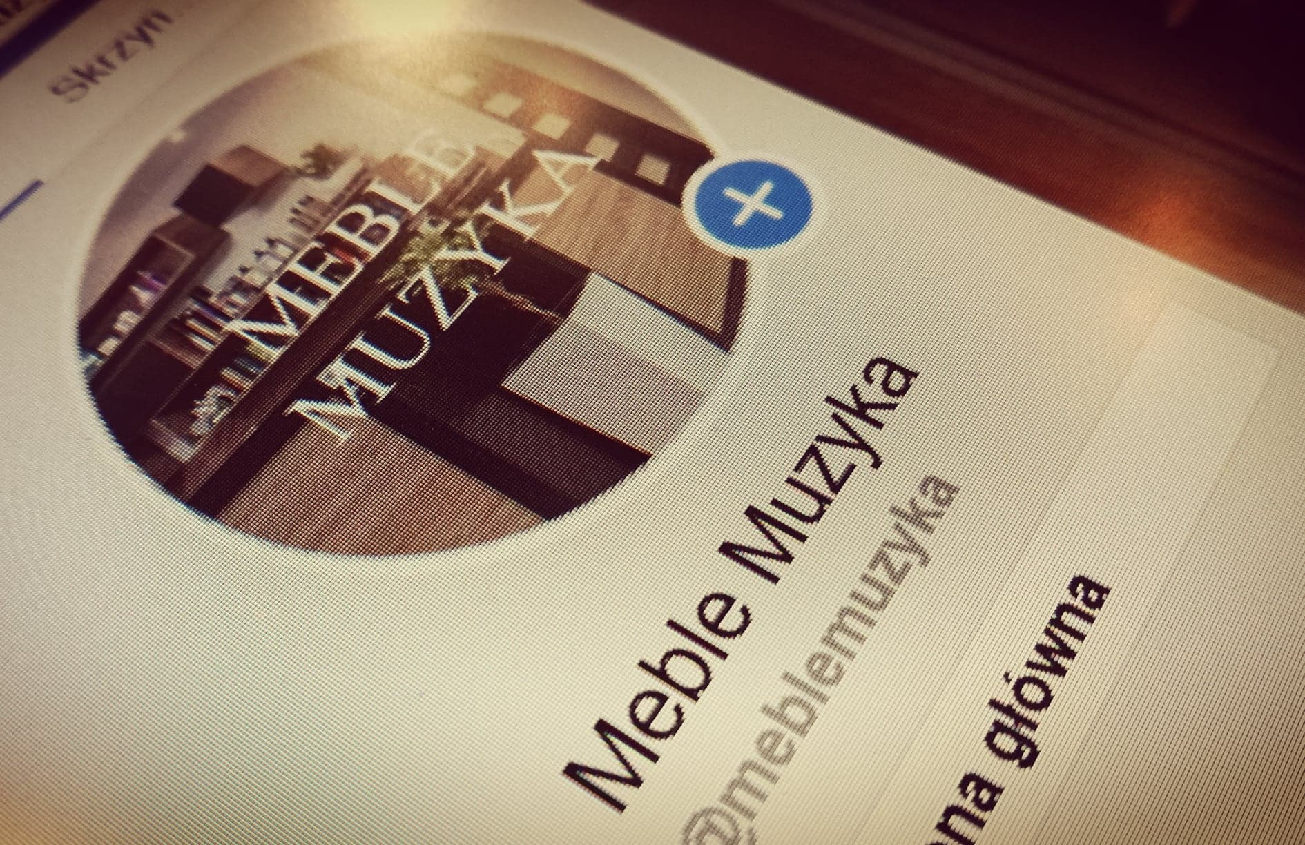 Ekran urządzenia z widocznym profilem firmy 'Meble Muzyka', prezentującym logo z regałem i napisem.