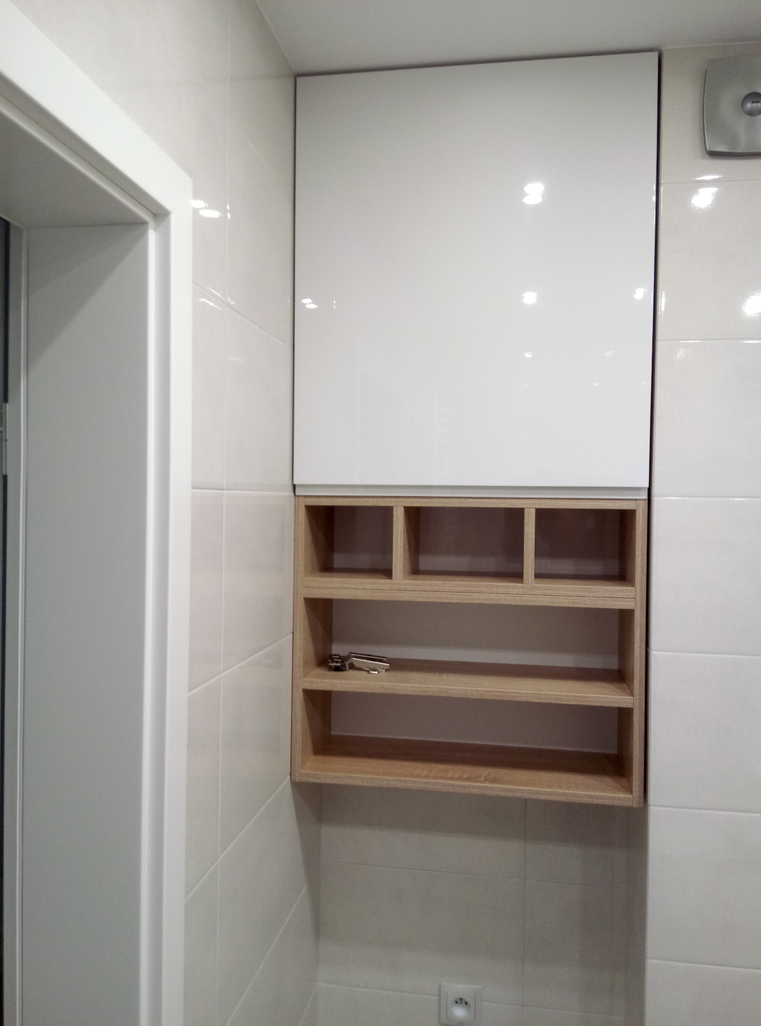 Szafka łazienkowa na wymiar z białym, lakierowanym frontem i drewnianymi półkami w Majdanie Krasienińskim, zamontowana nad gniazdkiem elektrycznym.