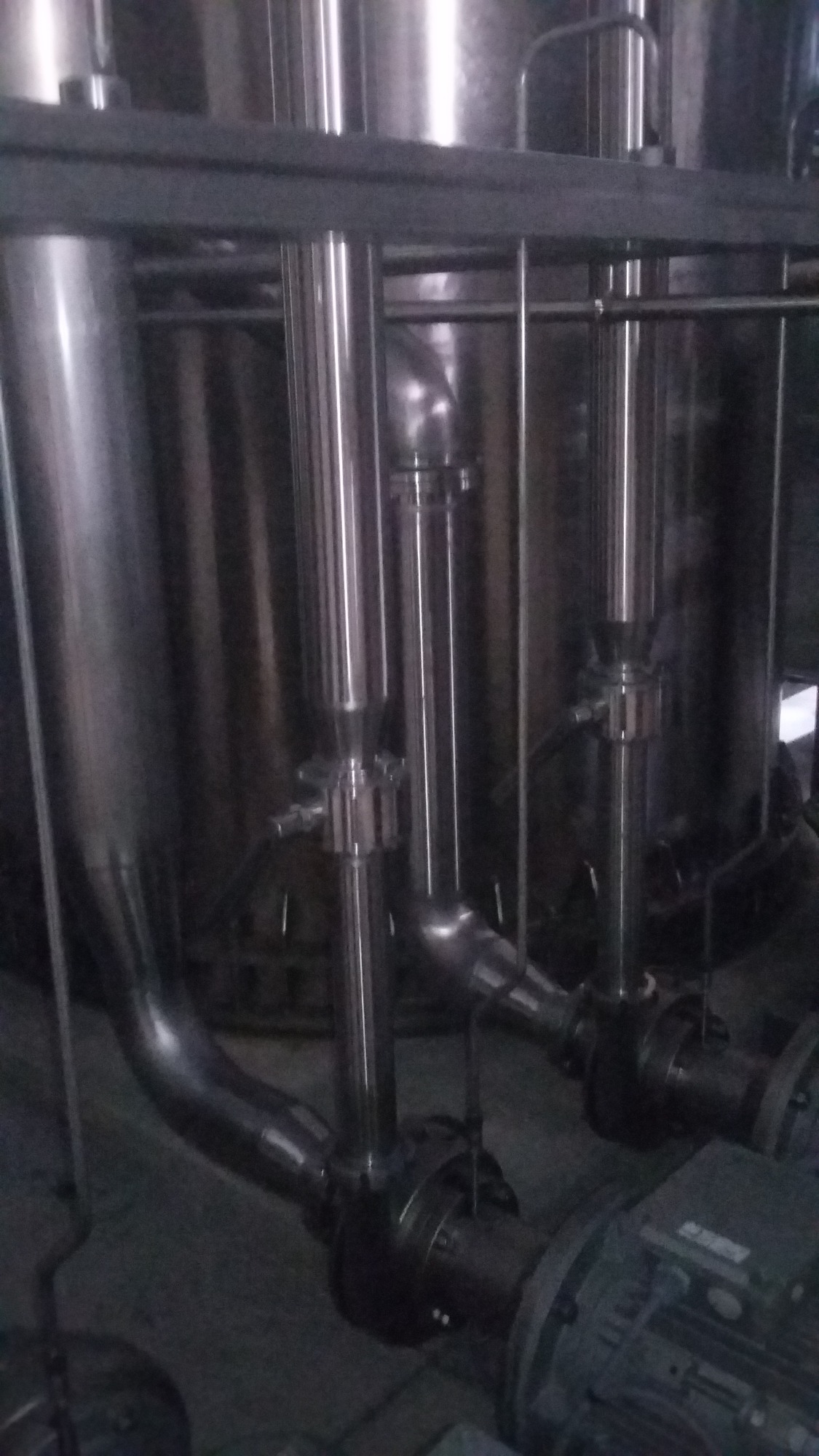 Błyszczące, metalowe rury i zbiorniki w pomieszczeniu przemysłowym, widoczne elementy instalacji technologicznej.