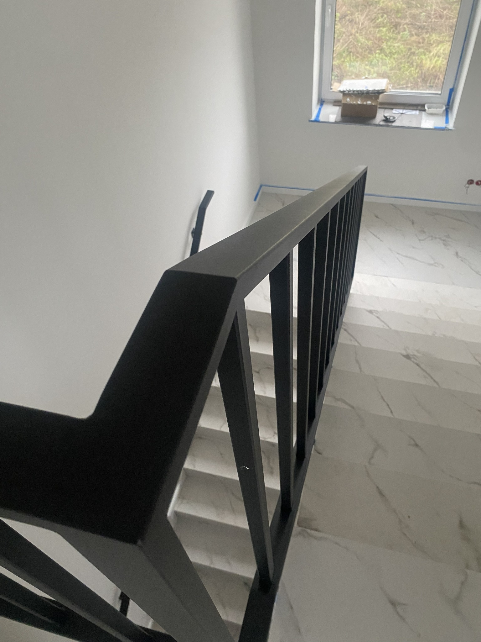 Nowoczesna, czarna balustrada schodowa z metalu, widok z góry na marmurowe schody. Minimalistyczny design, jasne wnętrze z oknem dachowym.