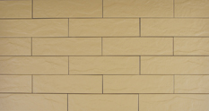 Detal ściany wykończonej beżowymi, prostokątnymi płytkami elewacyjnymi CERRAD z subtelną fakturą imitującą kamień naturalny, ułożonymi w regularny wzór z przesunięciem.